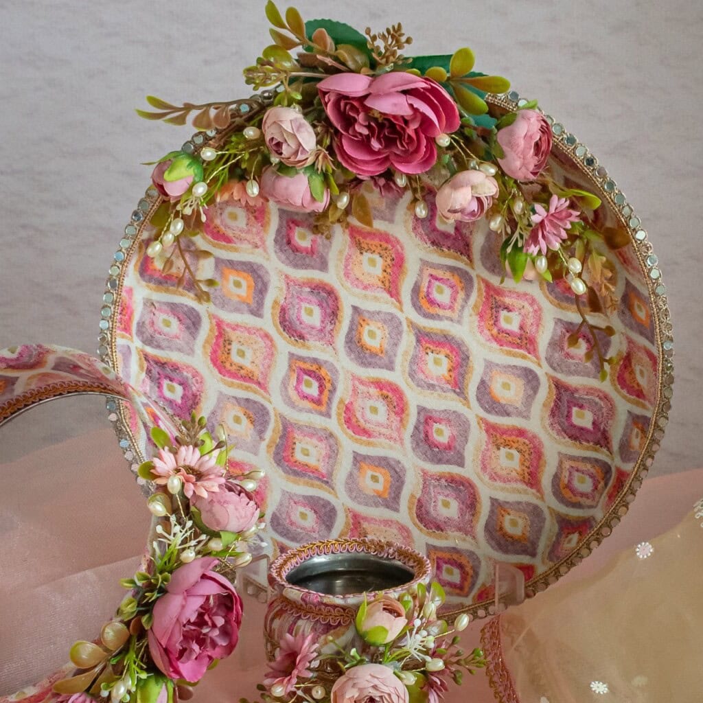 Floral Art presents A decorative round tray and accessories adorned with pink artificial flowers and green leaves, featuring a geometric patterned background.