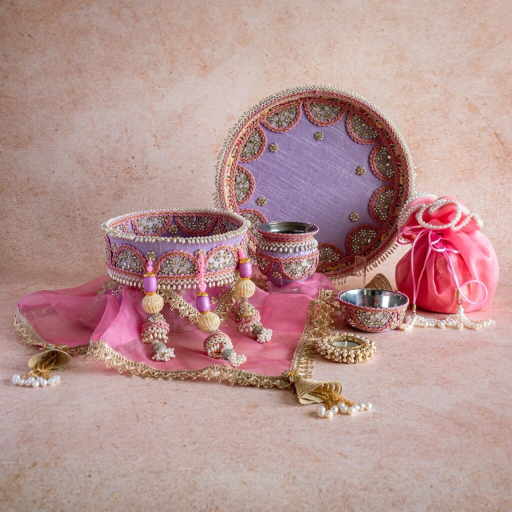 Floral Art presents A set of traditional Indian bridal accessories including a decorated tray, bangles, a potli bag, vessels, and a pink embellished dupatta displayed on a beige surface.