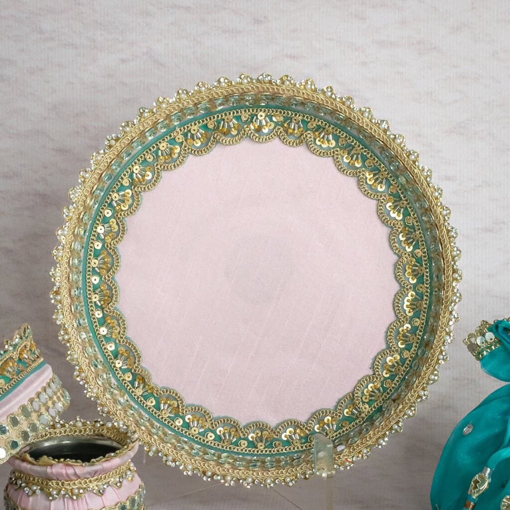 Floral Art presents A round decorative plate with gold and teal ornate edges on a light pink surface, displayed upright; the words "floral art" are written in the center.