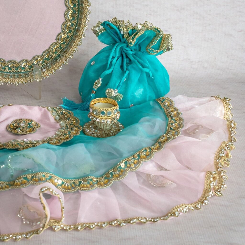 Floral Art presents A teal drawstring pouch, a decorative ring, and pink cloth with gold and turquoise trim displayed on a light surface.