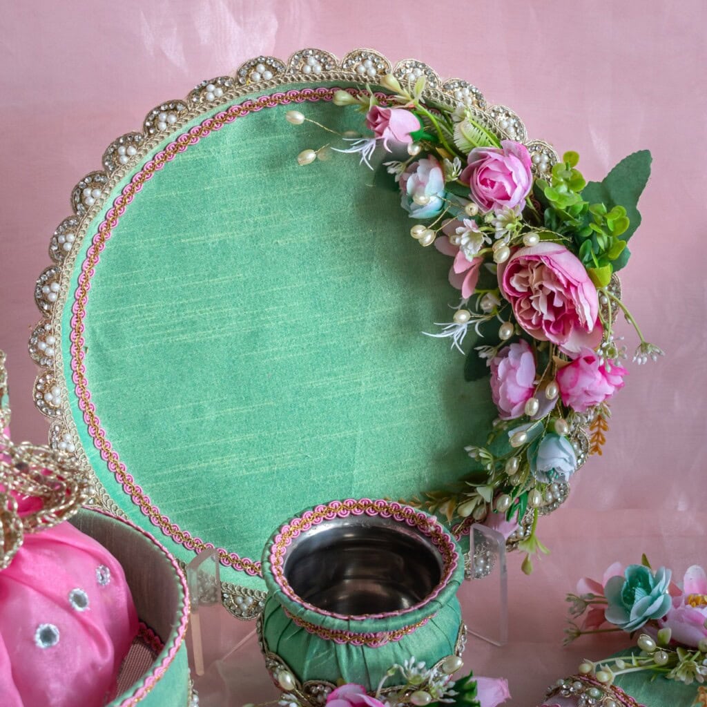 Floral Art presents A decorative green platter with ornate gold trim and artificial pink and white flowers, accompanied by a matching green and silver cup, set against a pink background.