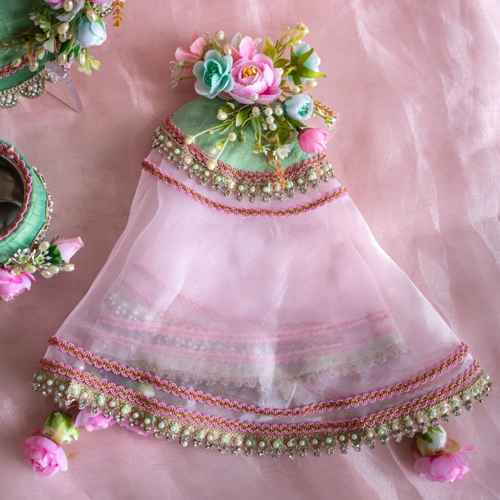 Floral Art presents A delicate pink and green dress with floral decorations and bead embellishments is displayed on a pink fabric background.