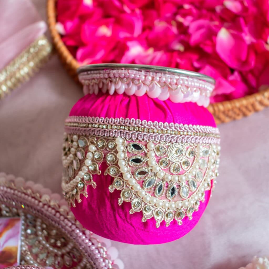 Floral Art presents A decorative pink pot adorned with intricate silver and pearl beadwork is placed near a basket filled with pink rose petals.