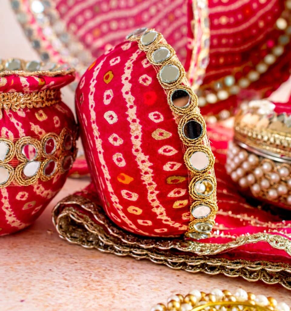 Floral Art presents Red and gold decorative fabric containers and trays with mirror and bead embellishments, arranged on a flat surface.