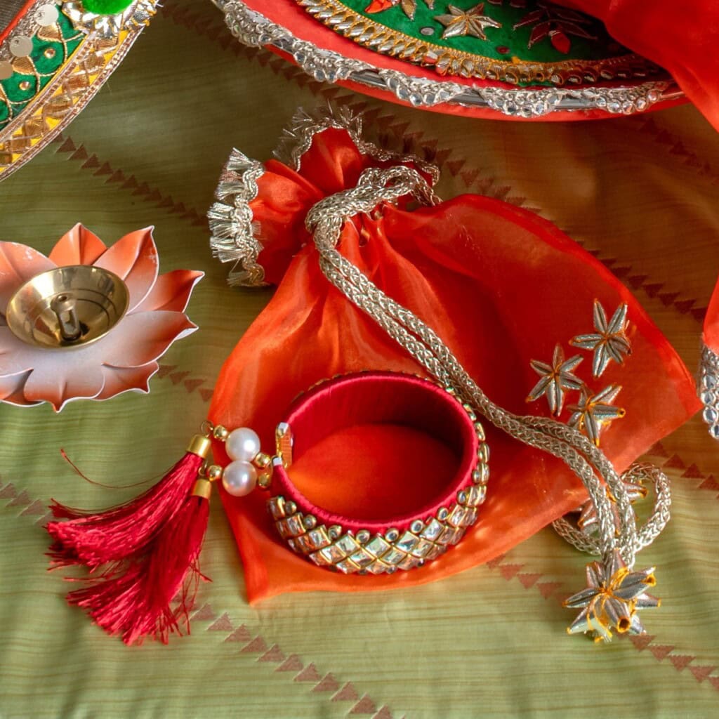 Floral Art presents A red and gold bangle, decorative pouch, and lotus shaped tealight holder are arranged on a green fabric with embroidery.