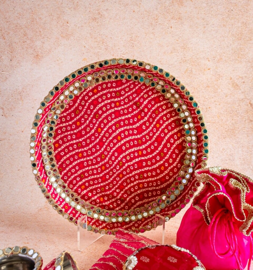 Floral Art presents Decorative round red tray with gold and gem accents, accompanied by a matching red and gold pouch, set against a neutral background.