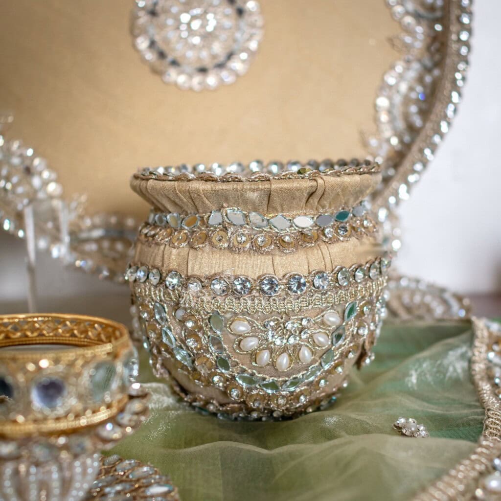 Floral Art presents A decorative pot adorned with pearls and sparkling stones, displayed on green fabric beside matching ornate items.