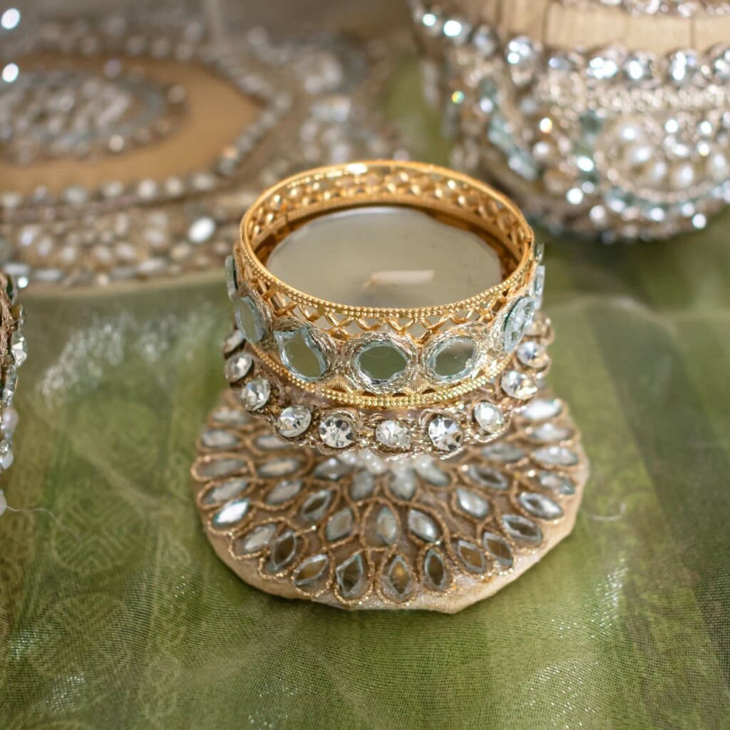 Floral Art presents A decorative glass candle holder embellished with gold metal and clear gemstones, placed on a matching ornate coaster atop green fabric.