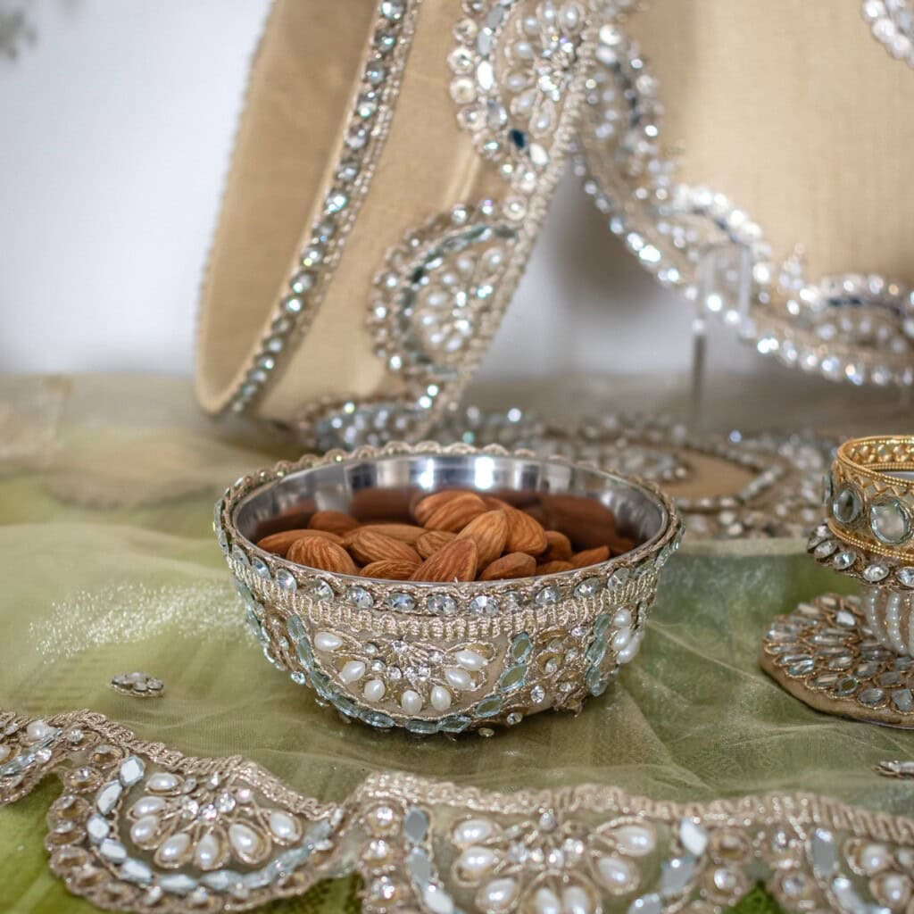 Floral Art presents A decorative silver bowl filled with almonds sits on an embroidered cloth, surrounded by ornate, beaded accessories and fabric.