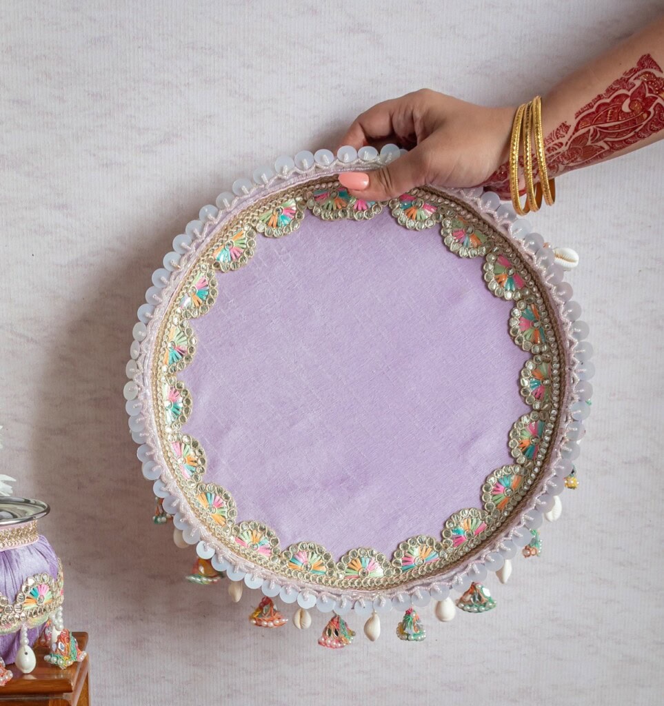 Floral Art presents A hand holding a round, lavender decorative tray with ornate bead and sequin trim, against a light background.
